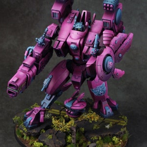 May include: A pink and grey painted miniature robot with a cat symbol on its leg. The robot has two large guns on its arms and a smaller gun on its left arm. The robot is standing on a base with a grey and brown surface.