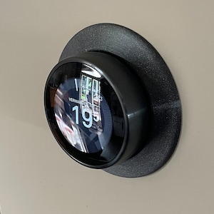 Puede incluir: Un termostato redondo negro con una pantalla digital que muestra una temperatura de 19 grados. El termostato está montado en una pared.