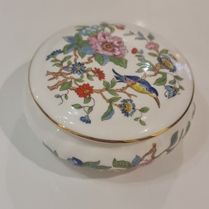 May include: A white porcelain trinket box with a floral design and a blue bird. The lid has a gold trim.