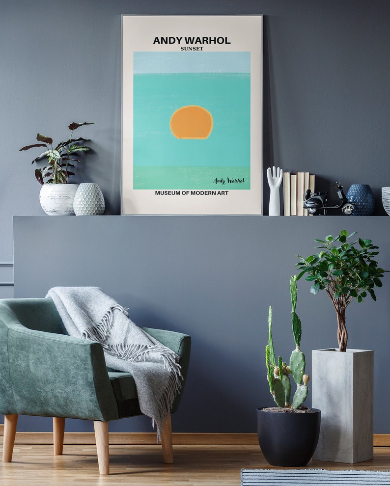 May include: A framed print of a sunset painting by Andy Warhol. The painting is a simple design of a yellow sun on a blue and green background. The text "Andy Warhol" and "Museum of Modern Art" are printed below the painting.