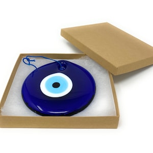 May include: A blue glass evil eye charm with a white and black eye, hanging from a blue string, in a brown cardboard box with white tissue paper.