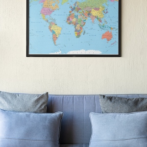 K&ouml;nnte beinhalten: Ein blaues Sofa mit drei Kissen, von denen zwei hellblau und eines dunkelgrau sind. Das Sofa steht vor einer Wand mit einer gerahmten Weltkarte, die daran h&auml;ngt. Auf einem Marmortisch vor dem Sofa stehen zwei Kerzen.