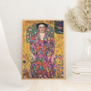 May include: A framed painting of a woman in a colourful floral dress standing against a gold background. The woman has dark hair and is wearing a necklace. The painting is surrounded by a wooden frame.