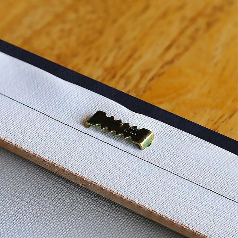 Peut inclure: Gros plan d'un cintre en dents de scie en m&eacute;tal dor&eacute; fix&eacute; &agrave; l'arri&egrave;re d'une toile.