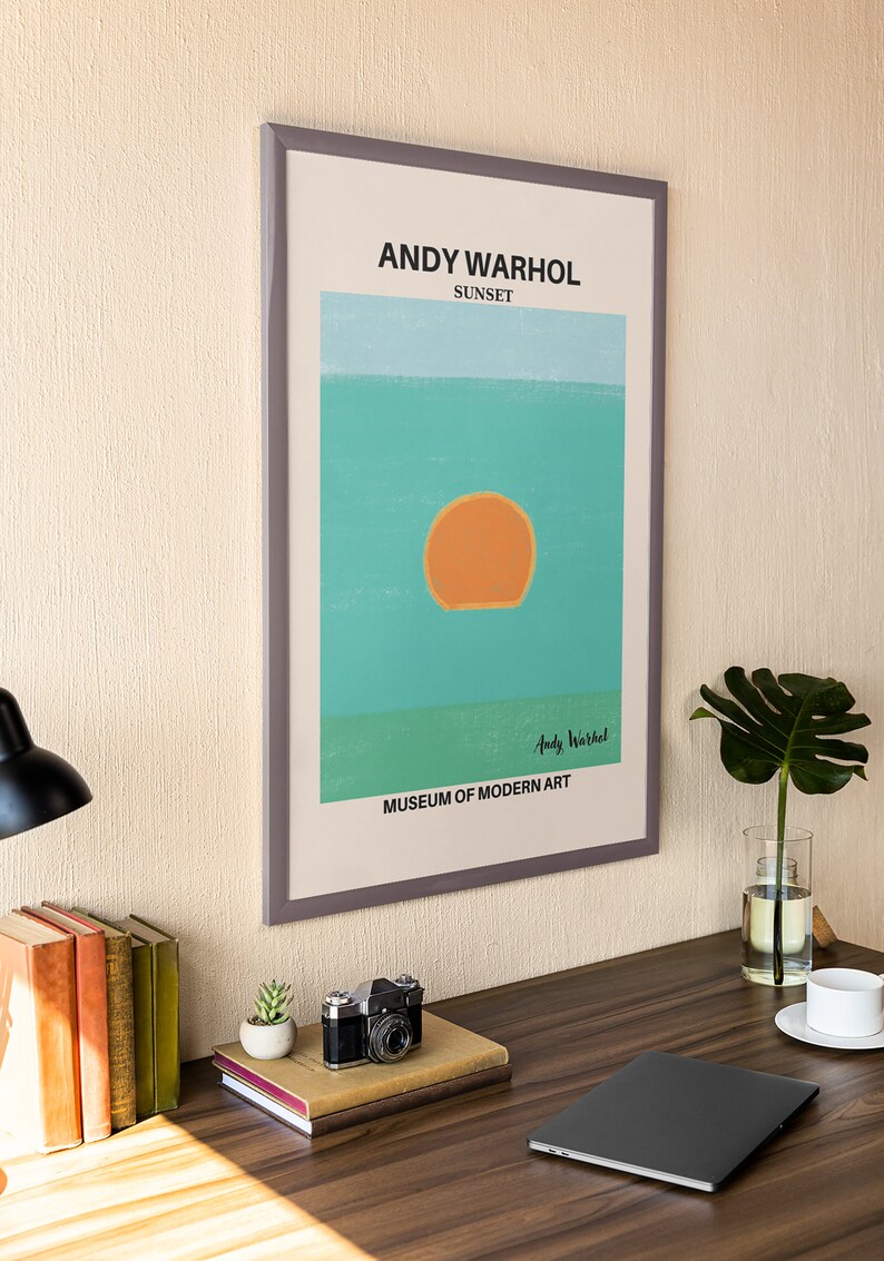 May include: A framed print of a sunset painting by Andy Warhol. The painting is a simple design of a large orange sun setting over a turquoise ocean. The text "Andy Warhol" and "Museum of Modern Art" are printed below the painting.