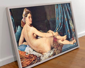 May include: A framed canvas print of the Grande Odalisque painting, featuring a reclining figure with a patterned headpiece, draped in blue curtains and orange fabric, set within a light-colored wooden frame resting on a wooden floor.
