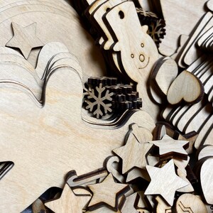 May include: A collection of unfinished wooden Christmas ornaments in various shapes, including stars, snowmen, mittens, and snowflakes. The ornaments are made of light-colored wood and are ready for painting or decorating. The image is a close-up shot.