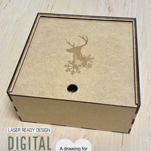 May include: A square wooden gift box with a laser-cut deer and snowflake design on the lid. The box is light brown with dark brown trim. Text on the image reads "LASER READY DESIGN DIGITAL DOWNLOAD SVG, AI, DXF, PDF" and "A drawing for the gift box is included!"