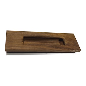 May include: A rectangular wooden drawer pull with a recessed handle. The pull is made of dark brown wood and has a smooth, polished finish. The handle is a rectangular cutout in the centre of the pull. The brand name "COHSAR" is visible on the right side.