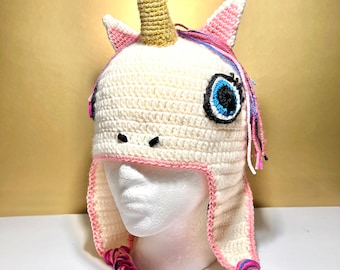 May include: White crocheted unicorn hat with a pink and blue braided tail. The hat has a gold horn and a blue eye with eyelashes.