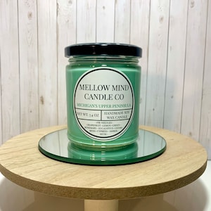 Puede incluir: Un tarro de vela de vidrio verde con una tapa negra. La etiqueta dice "MELLOW MIND CANDLE CO" y "MICHIGAN'S UPPER PENINSULA". La vela es de cera de soja hecha a mano y tiene un peso neto de 7,4 onzas. Las notas de aroma son agujas de pino, pomelo, lim&oacute;n, verde, romero, eucalipto, cedro, musgo, cipr&eacute;s, &aacute;mbar y almizcle.