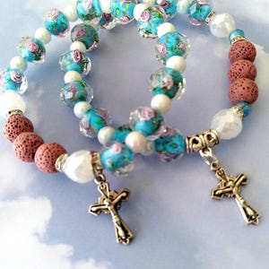 May include: Two bracelets with floral glass beads, white beads, and brown lava rock beads. Each bracelet has a silver cross charm.