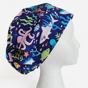 May include: A blue scrub hat with a colorful sea life pattern. The pattern includes fish, an octopus, seaweed, and coral.