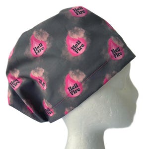 May include: Gray scrub hat with a pink and black repeating pattern of flames and the text "Hell Fire".