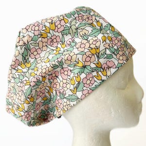 May include: A white scrub hat with a floral print featuring pink, yellow, and green flowers. The hat is made of a soft, comfortable fabric and is perfect for nurses, doctors, and other healthcare professionals.