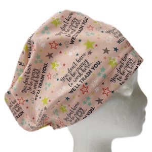 May include: Pink scrub hat with a repeating pattern of stars and the text "You don't have to be crazy to work here... We'll train you."