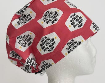 May include: A red surgical scrub cap with a repeating pattern of white speech bubbles containing the text "Quick Question... Are You For Real Right Now?" and yellow stars. The cap is designed to fit snugly on the head.