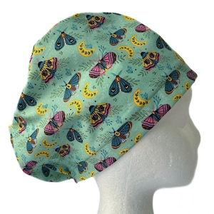 May include: A green scrub hat with a pattern of colorful moths and crescent moons.