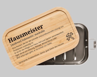 Könnte beinhalten: Eine Holz-Lunchbox mit einem Edelstahl-Innenraum. Der Deckel hat eine Definition des Wortes "Hausmeister" eingraviert, was ein deutsches Wort für "Hausmeister" ist.