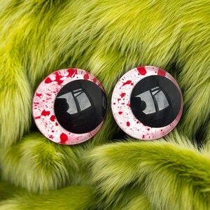 K&ouml;nnte beinhalten: Zwei runde, gl&auml;nzende, schwarz-rote Augen mit einem Blutspritzer-Design. Die Augen sind vor einem Hintergrund aus langem, limettengr&uuml;nem Kunstfell platziert. Die Augen haben eine reflektierende Oberfl&auml;che.