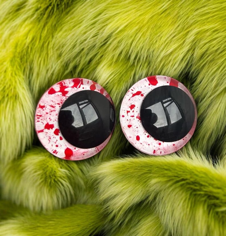 K&ouml;nnte beinhalten: Zwei runde, gl&auml;nzende, schwarz-rote Augen mit einem Blutspritzer-Design. Die Augen sind vor einem Hintergrund aus langem, limettengr&uuml;nem Kunstfell platziert. Die Augen haben eine reflektierende Oberfl&auml;che.
