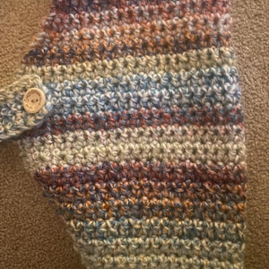 May include: A multi-coloured crocheted scarf with a brown button that says "Handmade with love".