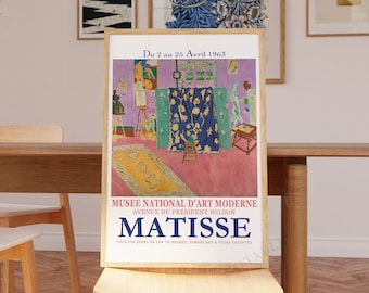 May include: A vintage poster advertising an exhibition of Matisse's work at the Musée National d'Art Moderne in Paris, France. The poster features a colorful painting of a room with a rug, furniture, and figures. The text on the poster reads "Du 2 au 25 Avril 1963", "Musée National d'Art Moderne", "Avenue du Président Wilson", "Matisse", and "Tous les jours de 10 à 18 heures, dimanches & fêtes exceptés".
