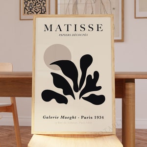May include: A black and white poster with the text "MATISSE PAPIERS DECOUPES" and a black abstract design of a plant with a beige circle in the background. The text "Galerie Maeght - Paris 1934" is at the bottom of the poster.