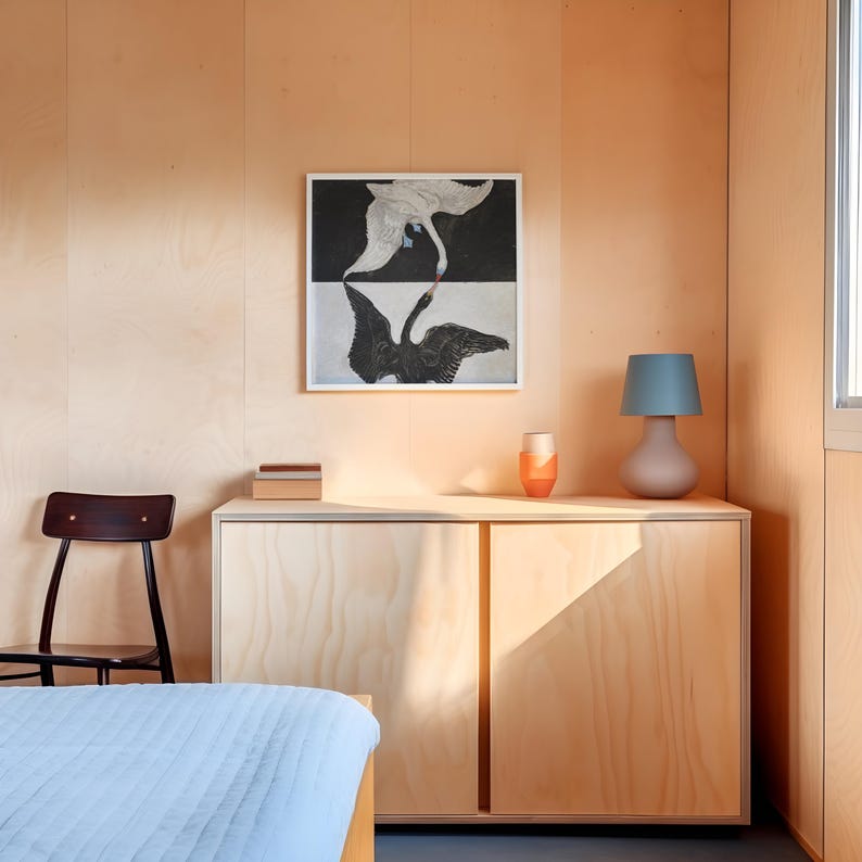 May include: A wooden cabinet with two doors, a lamp with a blue shade, and a vase with a red and orange design. A black and white print of two swans is hanging on the wall above the cabinet.