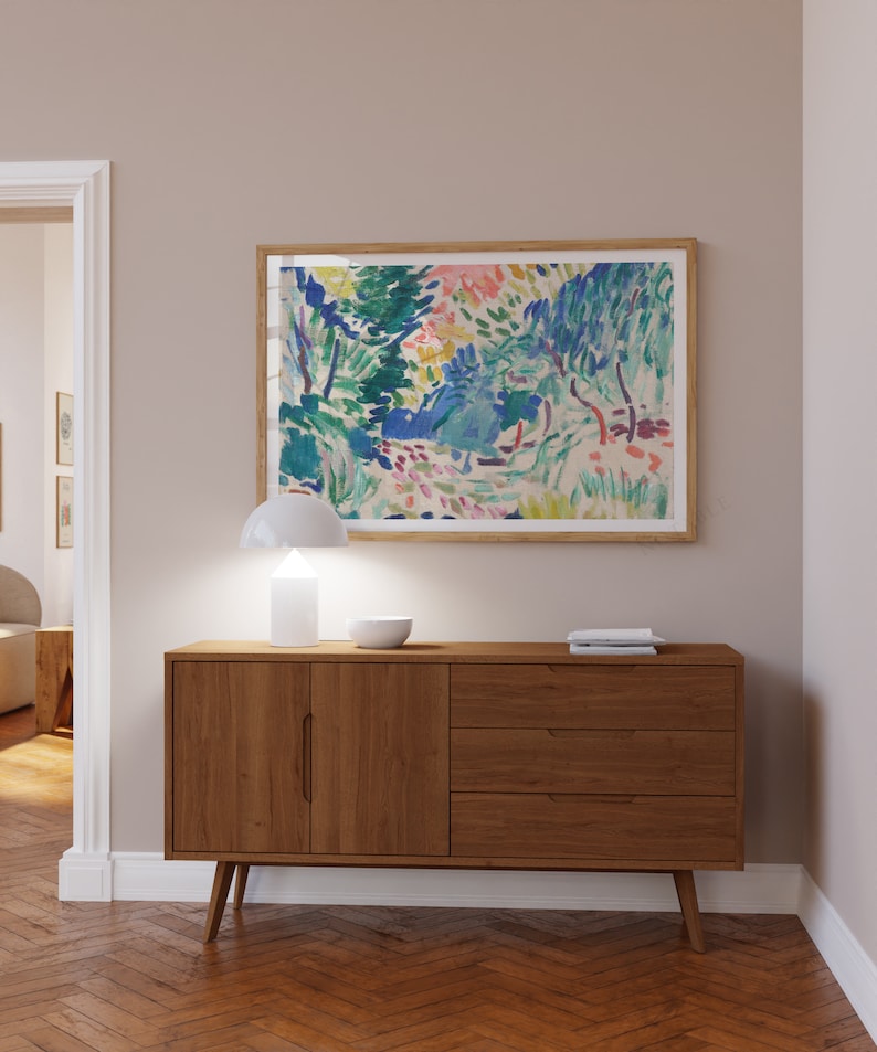 Pode incluir: Um aparador de madeira com duas portas e tr&ecirc;s gavetas. O aparador &eacute; de estilo moderno de meados do s&eacute;culo com pernas afiladas. Uma l&acirc;mpada branca e uma tigela branca est&atilde;o em cima do aparador. Uma pintura emoldurada de uma paisagem colorida est&aacute; na parede acima do aparador.