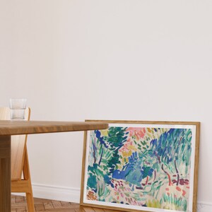 Pode incluir: Uma pintura abstrata enquadrada com uma cena de paisagem colorida. A pintura apresenta uma variedade de tons de azul, verde, rosa e amarelo. A pintura &eacute; enquadrada em uma moldura de madeira natural.