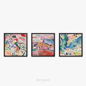 May include: Three framed paintings in a row. The leftmost painting features a woman in a colorful dress standing in a landscape with pink, green, and blue hues. The middle painting shows a pink building with a blue roof in a landscape with blue water and green hills. The rightmost painting shows a landscape with green and blue trees and a path.