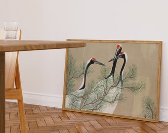 Puede incluir: Una impresión enmarcada de una pintura de estilo japonés que representa tres grullas blancas con alas negras y detalles rojos posadas en una rama de pino. El fondo es de color beige claro.