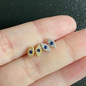 May include: Four pairs of small stud earrings. Two pairs are gold-toned with a central blue stone and surrounding clear stones. The other two pairs are silver-toned with a central blue stone and surrounding clear stones.
