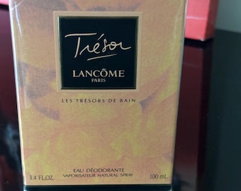 Puede incluir: Una caja rectangular de Lancôme Trésor Eau Déodorante, envuelta en plástico transparente. La caja tiene un diseño floral dorado y melocotón. La parte frontal muestra el nombre de la marca y los detalles del producto, incluyendo "3.4 FL OZ" y "100 mL".