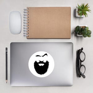 Puede incluir: Una pegatina en blanco y negro de la cara de un hombre con barba. La pegatina está en un portátil plateado.