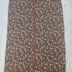 Puede incluir: Prenda sin mangas y larga, con un estampado floral en tonos rosa, melocotón y amarillo sobre un fondo gris oscuro. La prenda tiene una cremallera de cuerpo entero en la parte delantera. La tela parece suave y ligera.