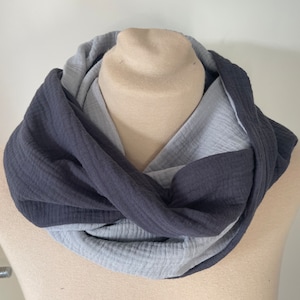 Puede incluir: Bufanda infinita de dos tonos en tonos grises y carbón. La bufanda está hecha de una tela suave y texturizada y está drapeada alrededor de una cabeza de maniquí. El diseño presenta un efecto en capas, con el gris más oscuro en el exterior y un gris más claro en el interior.