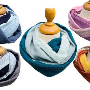 May include: Six colourful infinity scarves are displayed on mannequin heads. The scarves feature a variety of colours, including blues, greens, pinks, purples, and earth tones. The fabric appears to be a soft, lightweight material.