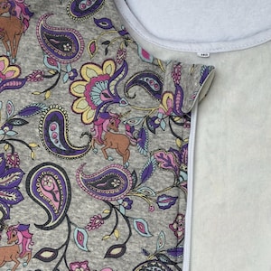 May include: A grey sleep sack featuring a paisley and unicorn pattern in shades of purple, pink, and brown. The design includes brown unicorns with pink manes and a white zipper. The sleep sack has a white interior and a tag that reads "160".