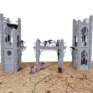 May include: A set of grey miniature gothic ruins featuring two tall towers and a central arched bridge structure. Several small, painted pink and black creature figurines are positioned on the bridge and around the base of the structures.