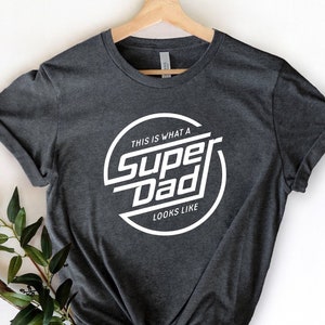 May include: A dark gray t-shirt with a white circle graphic that says "This is what a Super Dad looks like".