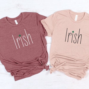 May include: Two t-shirts with the word "Irish" and a shamrock printed on them. The shirt on the left is heather mauve and the shirt on the right is heather peach.