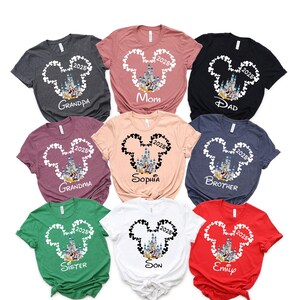 May include: Nine different t-shirts featuring a white Mickey Mouse head outline with a picture of Cinderella's castle inside. Each shirt has a different name printed on it, including "Grandpa", "Mom", "Dad", "Grandma", "Sophia", "Brother", "Sister", "Son", and "Emily".