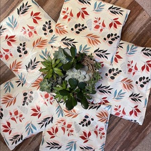 a potted plant with green leaves and a white vase filled with white flowers, placed on a wooden surface. The plant is surrounded by colorful patterned pillows.