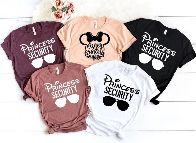 May include: Five t-shirts with different designs.  Two shirts are maroon with white text that says "Princess Security" and sunglasses. One shirt is peach with black text that says "Disney Princess" with a black Mickey Mouse head and bow. One shirt is black with white text that says "Princess Security" and sunglasses. One shirt is white with black text that says "Princess Security" and sunglasses.