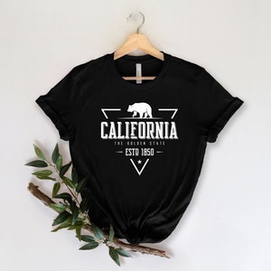 May include: Black t-shirt with a white graphic design featuring a bear, a triangle, and the text "California, The Golden State, Est. 1850".