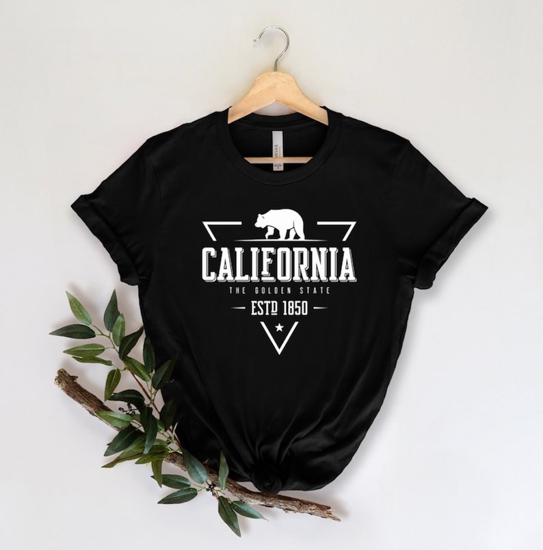May include: Black t-shirt with a white graphic design featuring a bear, a triangle, and the text "California, The Golden State, Est. 1850".