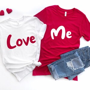 Puede incluir: Dos camisetas blancas con texto rojo. Una camiseta dice "Love" y la otra dice "Me".