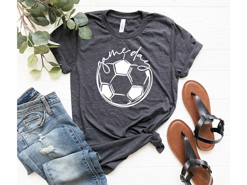 May include: A dark grey t-shirt with a white soccer ball graphic and the text "game day" in a cursive font.
